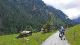 Unterwegs auf Tour - ein Mountainbiker fährt auf einer Forststraße umliegend ist die Bergwelt.