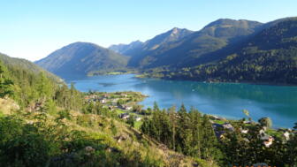 Der Weissensee - ein Highlight der E-MTB Transalp. Um den See erheben sich die Berge. Die Sonne scheint.