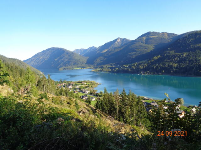 Der Weissensee - ein Highlight der E-MTB Transalp. Um den See erheben sich die Berge. Die Sonne scheint.