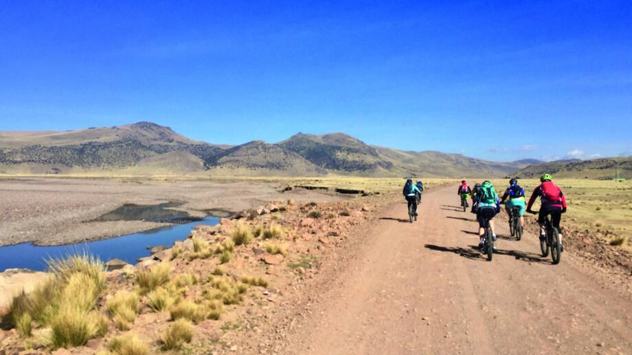 Ein MTB-Gruppe auf einer Sandpiste unterwegs. Die Gruppe ist auf einem Hochplateau unterwegs. Die Sonne scheint und der Himmel ist wolkenlos und blau.