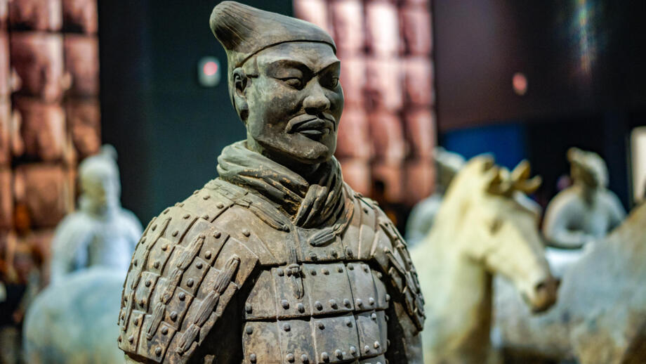 Ein Terracotta Krieger und Pferde im Hintergrund, aufgenommen im Museum