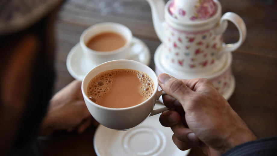 Hand hält Teetasse und weiteres Geschirr
