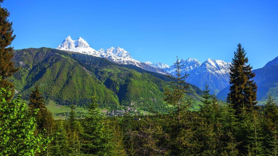 Dorf Ananuri in Swanetien in grünem Bergland mit vergletscherten Kaukasus-Gipfeln im Hintergrund
