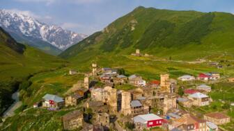 Ort Ushguli in Swanetien mit Häusern und Wehrtürmen in grüner Hügellandschaft mit vergletschertem Gebirge im Hintergrund
