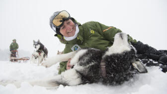 Eine junge Frau liegt im Schnee mit einem Husky