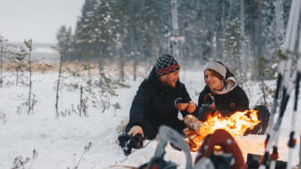 Zwei junge Erwachsene sitzen am Lagerfeuer im Schnee