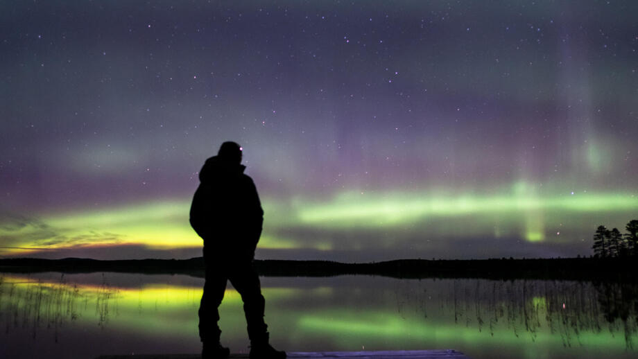 Ein Mann steht mit dem Rücken zur Kamera. Im Hintergrund tanzen grüne Polarlichter