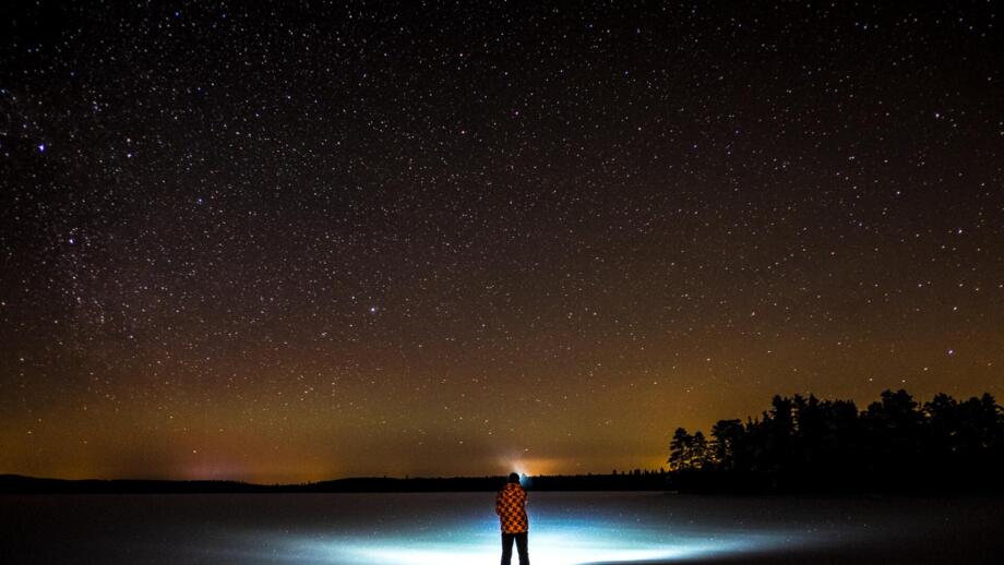 Eine Person mit Stirnlampe steht in der Nacht in Schwedisch Lappland