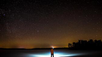 Eine Person mit Stirnlampe steht in der Nacht in Schwedisch Lappland