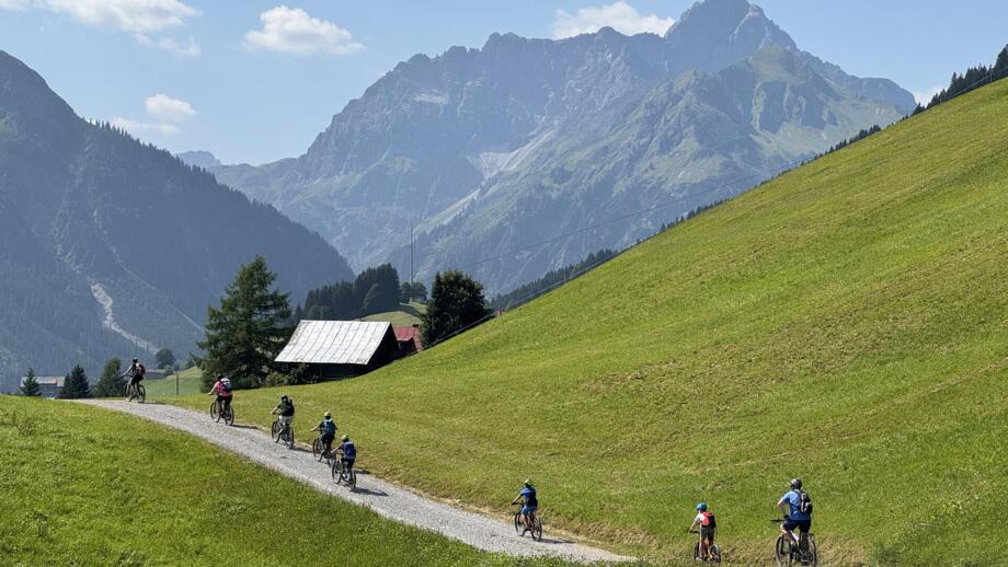 Eine MTB-Gruppe unterwegs auf Tour im Allgäu. Im Hintergrund ist die Allgäuer Bergwelt zu sehen. Der Himmel ist bewölkt.