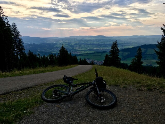 Ein Mountainbike liegt auf einer Almwiese. Vom Ausgangpunkt hat man eine Weitsicht. Der Himmel ist bewölkt.