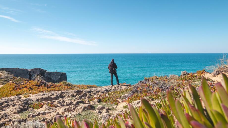 Wanderer mit Blick auf das Meer von Felsklippen bei Vila Nova de Milfontes