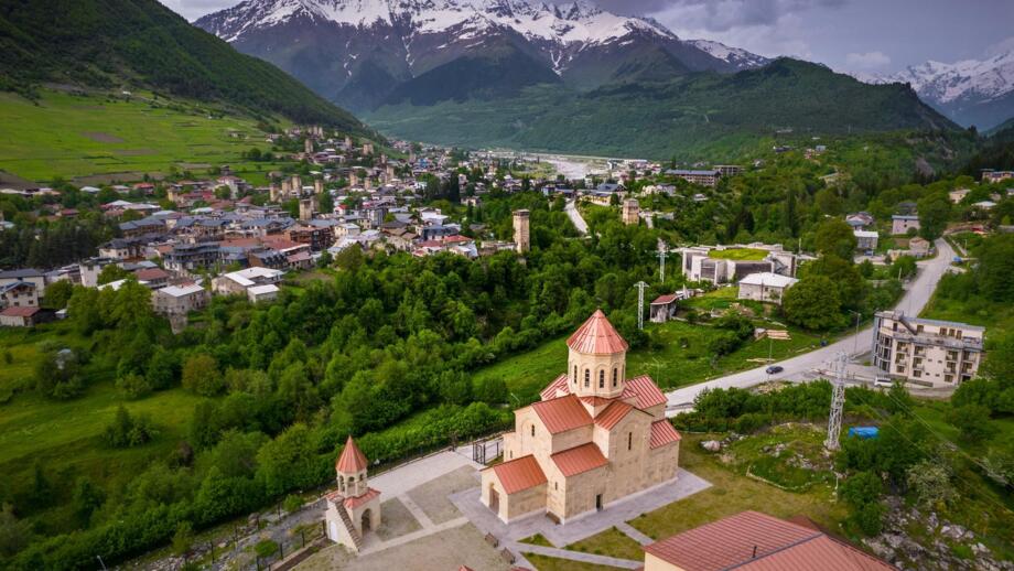 Luftaufnahme der Stadt Mestia mit den Bergen im Hintergrund und einem Kloster im Vordergrund