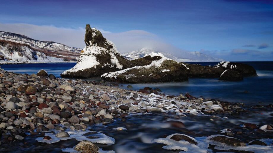 Küste des Ochotskischen meeres mit Felsen, Kieseln und etwas schnee auf der Insel Hokkaido