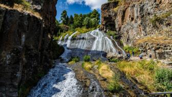 Wanderer unterwegs zu einem Wasserfall mit einer breiten Kaskade in einem Flusstal bei Jemuk in Armenien