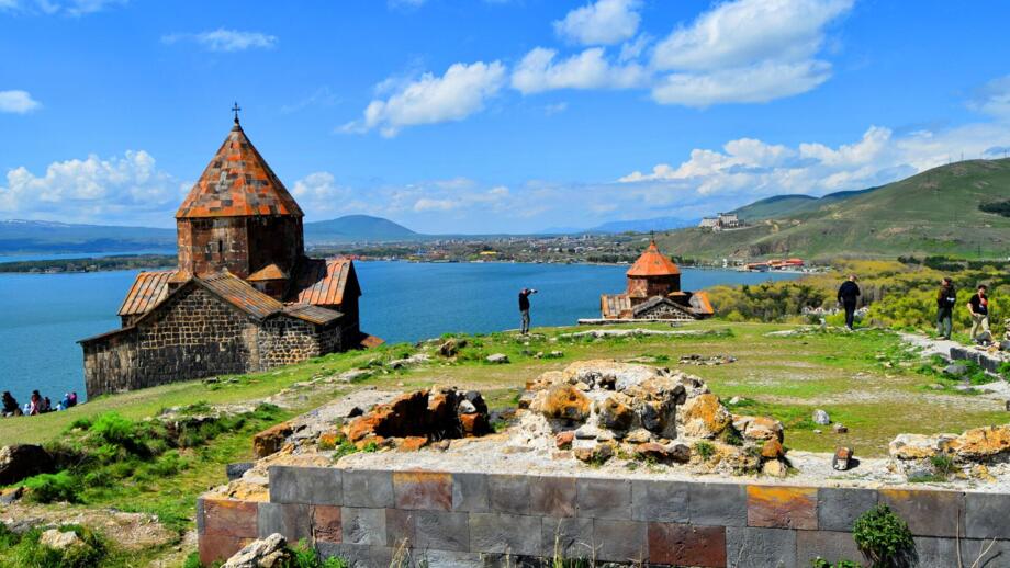 Zwei Kreuzkjuppelkirchen auf grünem Wiesengrund am tiefblauen Sevansee in Armenien