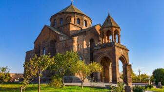 Hripsime-Kirche mit Kreuzkuppel in Vashgarapat im Sonnenlicht mig blauem Himmel und grüner Wiese im Vordergrund
