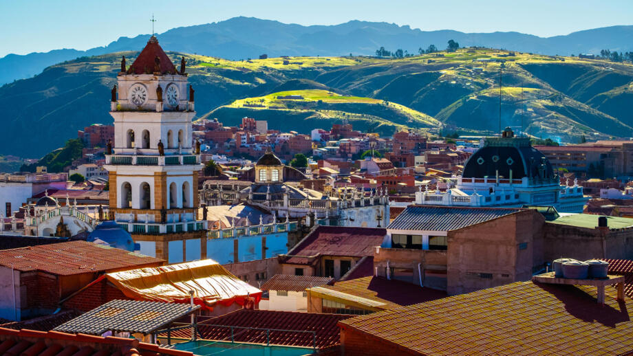 Blick über die kolonial geprägte Stadt Sucre in Bolivien mit dem Turm der Kathedrale und grünem Felder dahinter auf die Berge
