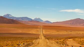 Wüstenpist auf rotem Sand in der Atacama mit Vulkanbergen im Hintergrund und blauem Himmel