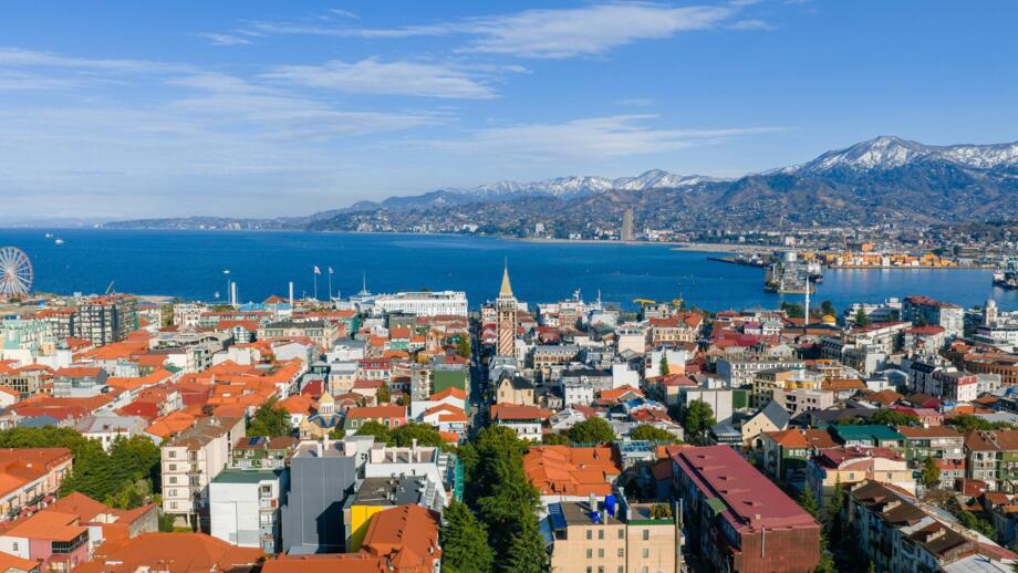 Blick über die Dächer der georgischen Stadt Batumi auf das Schwarze Meer und weiß gezuckerte Berghügel