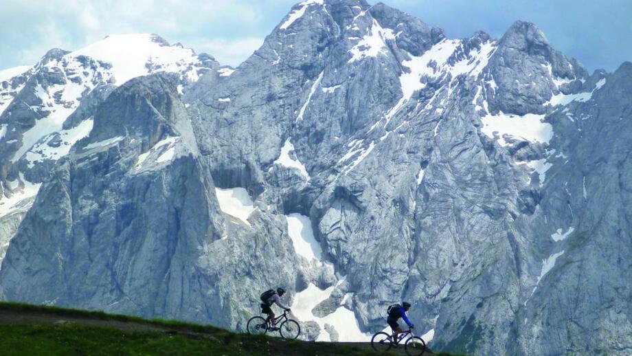 Zwei Mountainbiker unterwegs mit der imposanten Bergwelt der Dolomiten im Hintergrund.