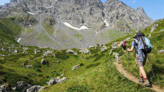 Zwei Wabdernde mit Hund in grünem Almgelände vor felsiger Gebirgskulisse in Georgien
