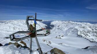Gipfelkreuz mit blauem Himmel und Bergpanorama